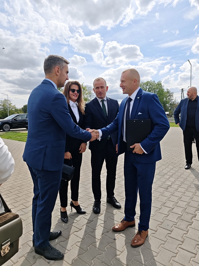 Uczestnicy uroczystości podczas powitania przed budynkiem SDOO Nowe Linie. Dyrektor SDOO podaje dłoń jednemu z gości.gromadzeni uczestnicy posiedzenia spotkali się w sali konferencyjnej Centrum Usług Publicznych w Gryficach. Zasiedli do stołu. Przyjęto porządek obrad.

