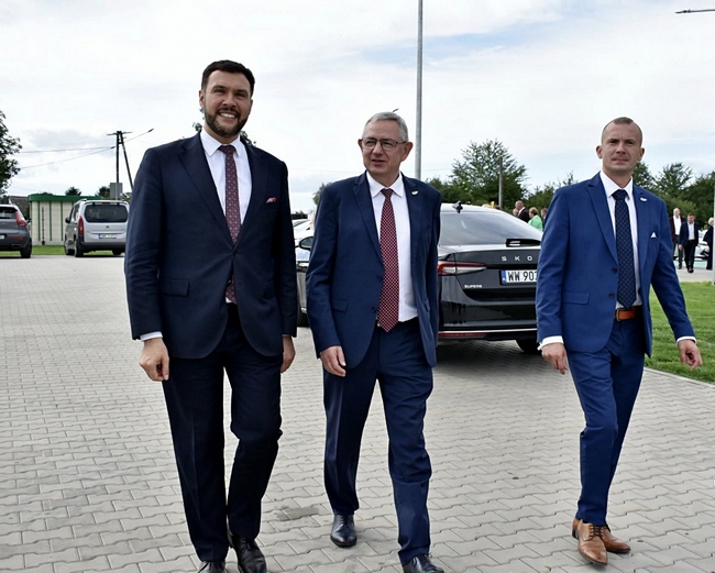 Wiceminister, Dyrektor COBORU oraz Dyrektor SDOO podczas zwiedzania terenu Stacji. W tle widoczne samochody oraz zabudowania gospodarstwa doświadczalnego.Zgromadzeni uczestnicy posiedzenia spotkali się w sali konferencyjnej Centrum Usług Publicznych w Gryficach. Zasiedli do stołu. Przyjęto porządek obrad.
