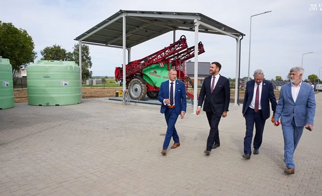 Wiceminister, Dyrektor COBORU, Dyrektor SDOO, Zastępca Dyrektora Departamentu Hodowli i Ochrony Roślin podczas zwiedzania zaplecza gospodarstwa. W tle znajduje się ciągnik rolniczy z opryskiwaczem oraz zbiorniki na wodę.Zgromadzeni uczestnicy posiedzenia spotkali się w sali konferencyjnej Centrum Usług Publicznych w Gryficach. Zasiedli do stołu. Przyjęto porządek obrad.
