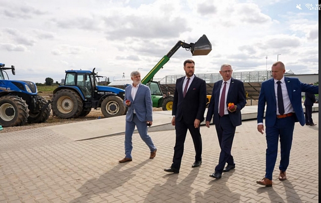 Wiceminister, Dyrektor COBORU, Dyrektor SDOO, Zastępca Dyrektora Departamentu Hodowli i Ochrony Roślin podczas zwiedzania zwiedzania infrastruktury rolniczej SDOO. W tle widoczne ciągniki, maszyny rolnicze oraz obiekty doświadczalne.
